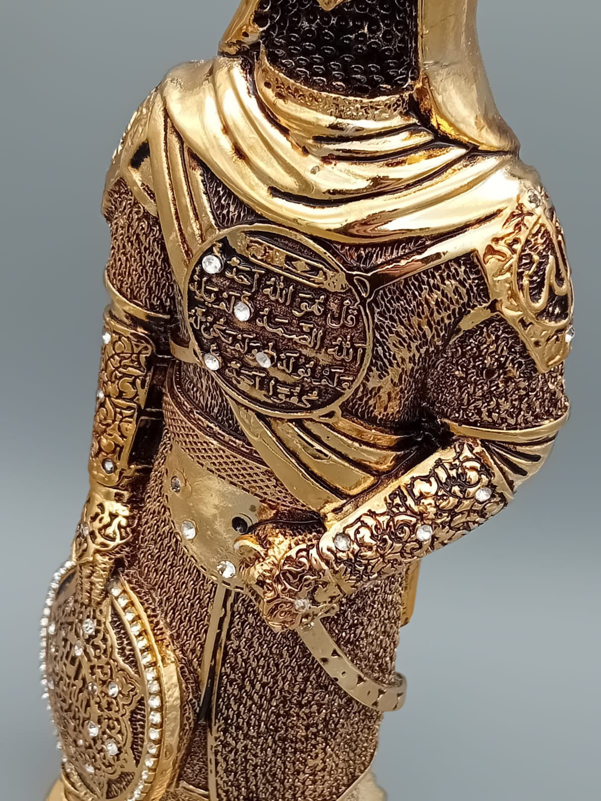 Statue dorée d’un soldat ottoman en armure, tenant un bouclier orné de calligraphie islamique, exposée sur une étagère en bois entourée de livres anciens