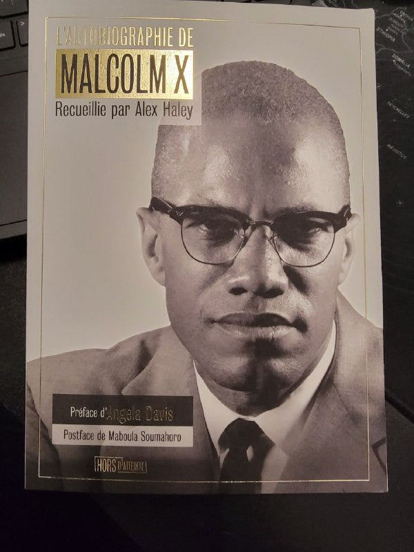 Couverture du livre L’autobiographie de Malcolm X, recueillie par Alex Haley, avec une photo en noir et blanc de Malcolm X portant des lunettes et un costume, posée sur une étagère en bois.