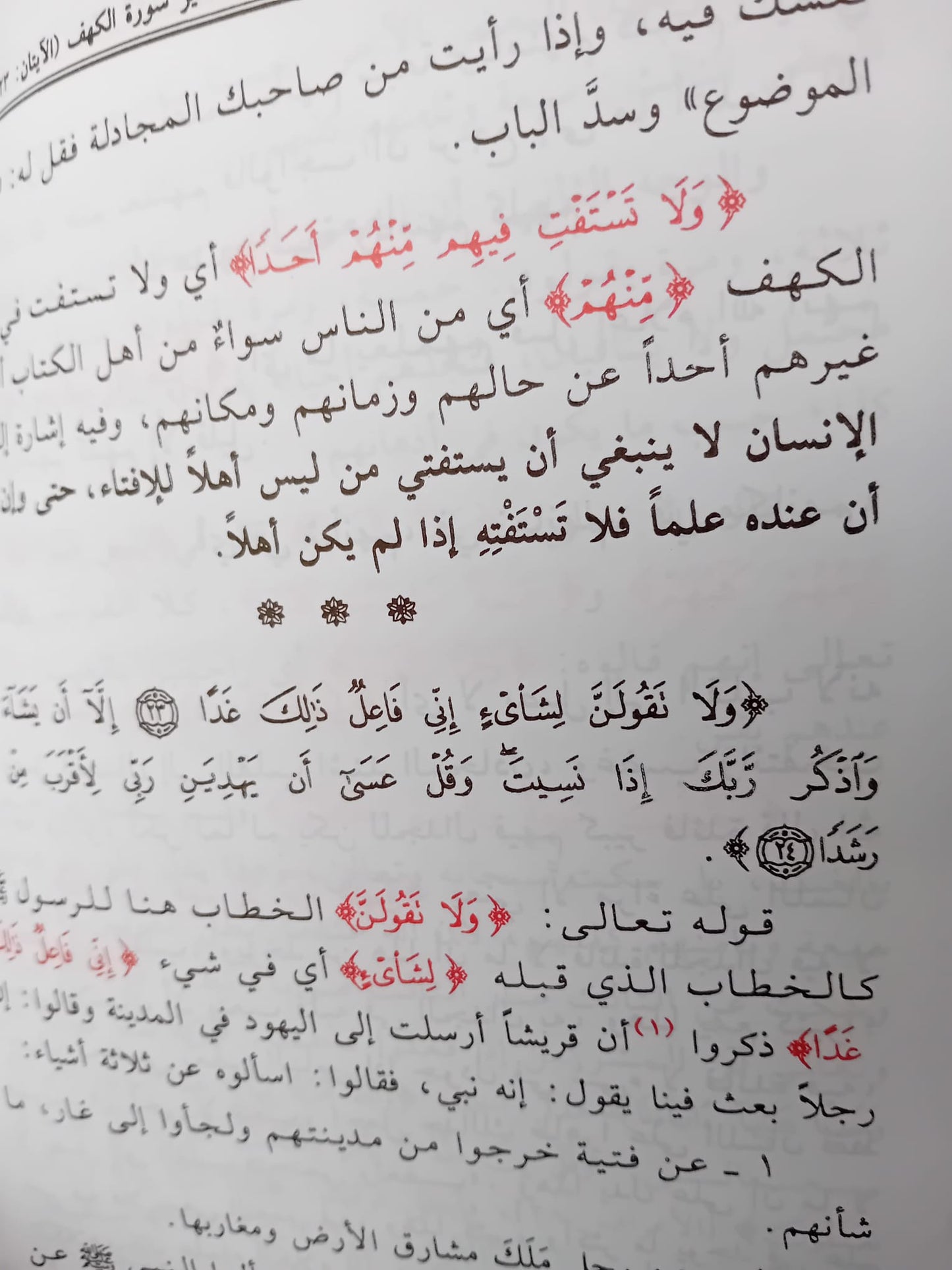 Photographie d’un livre en arabe intitulé Tafsir al-Qur'an al-Karim – Sourate al-Kahf du cheikh Muhammad ibn Salih al-‘Uthaymin, posé verticalement sur une surface claire. La couverture présente un fond crème et rose décoré de motifs islamiques et d'arabesques, avec une calligraphie soignée au centre
