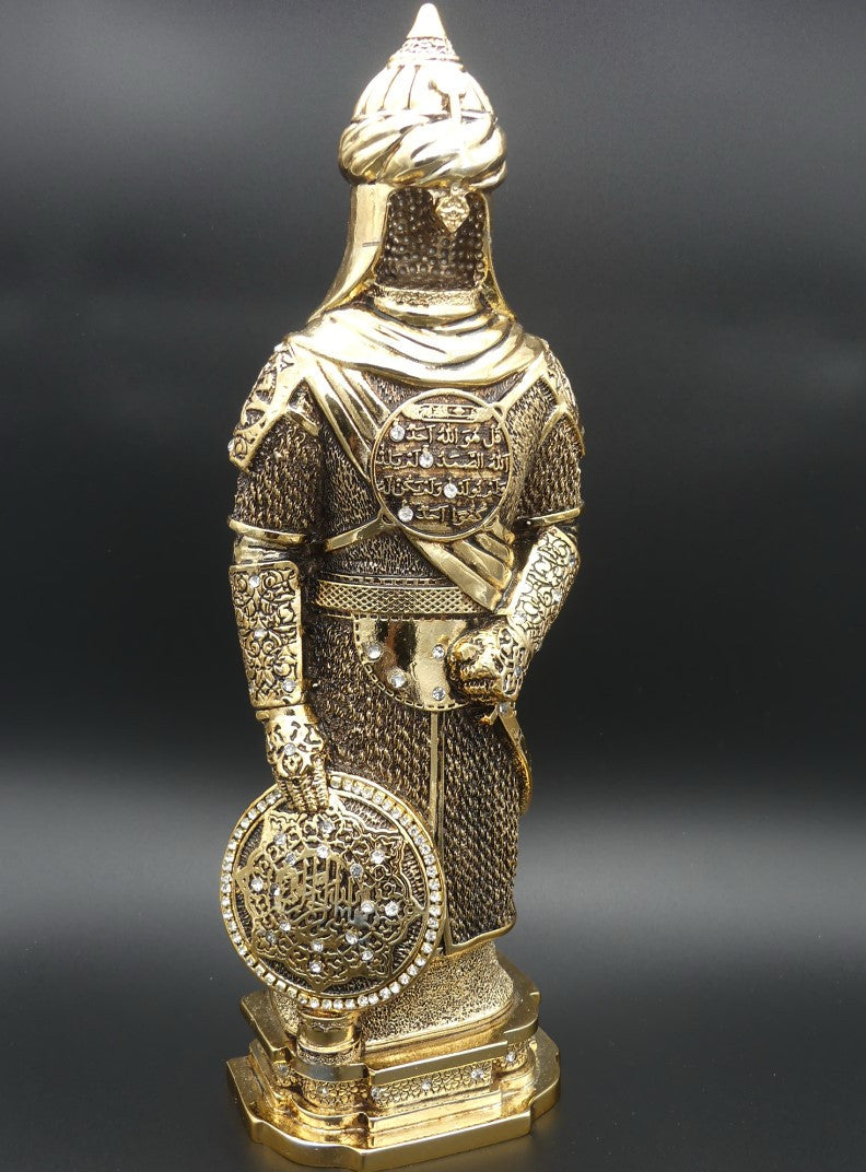 Statue dorée d’un soldat ottoman en armure, tenant un bouclier orné de calligraphie islamique, exposée sur une étagère en bois entourée de livres anciens